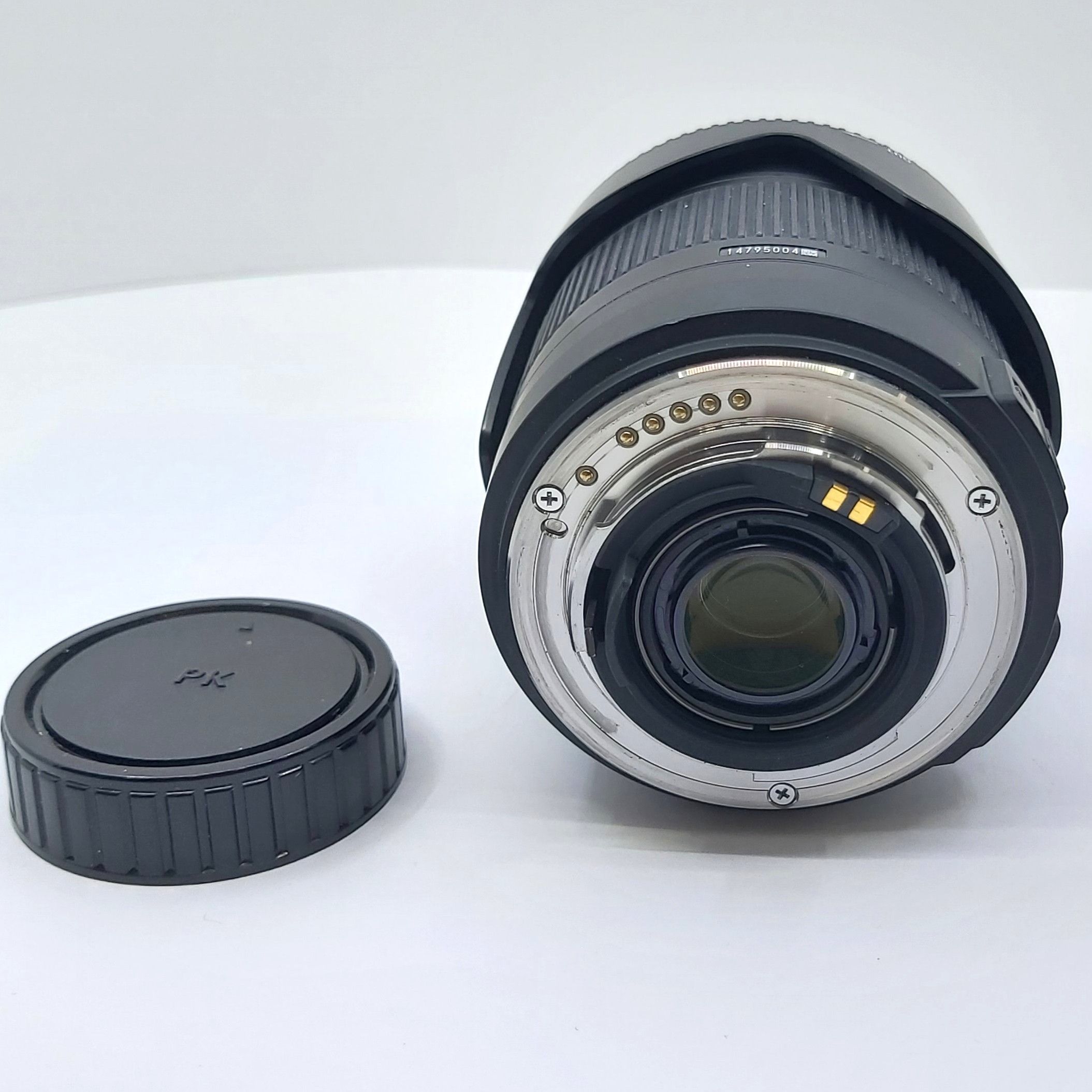 Sigma 18-250mm F3.5-6.3 DC Macro Objektiv für Pentax, Nahaufnahme vom Bajonett-Anschluss, daneben Objektivdeckel, schwarze Softtasche und Originalverpackung nicht im Bild, auf weißem Hintergrund.