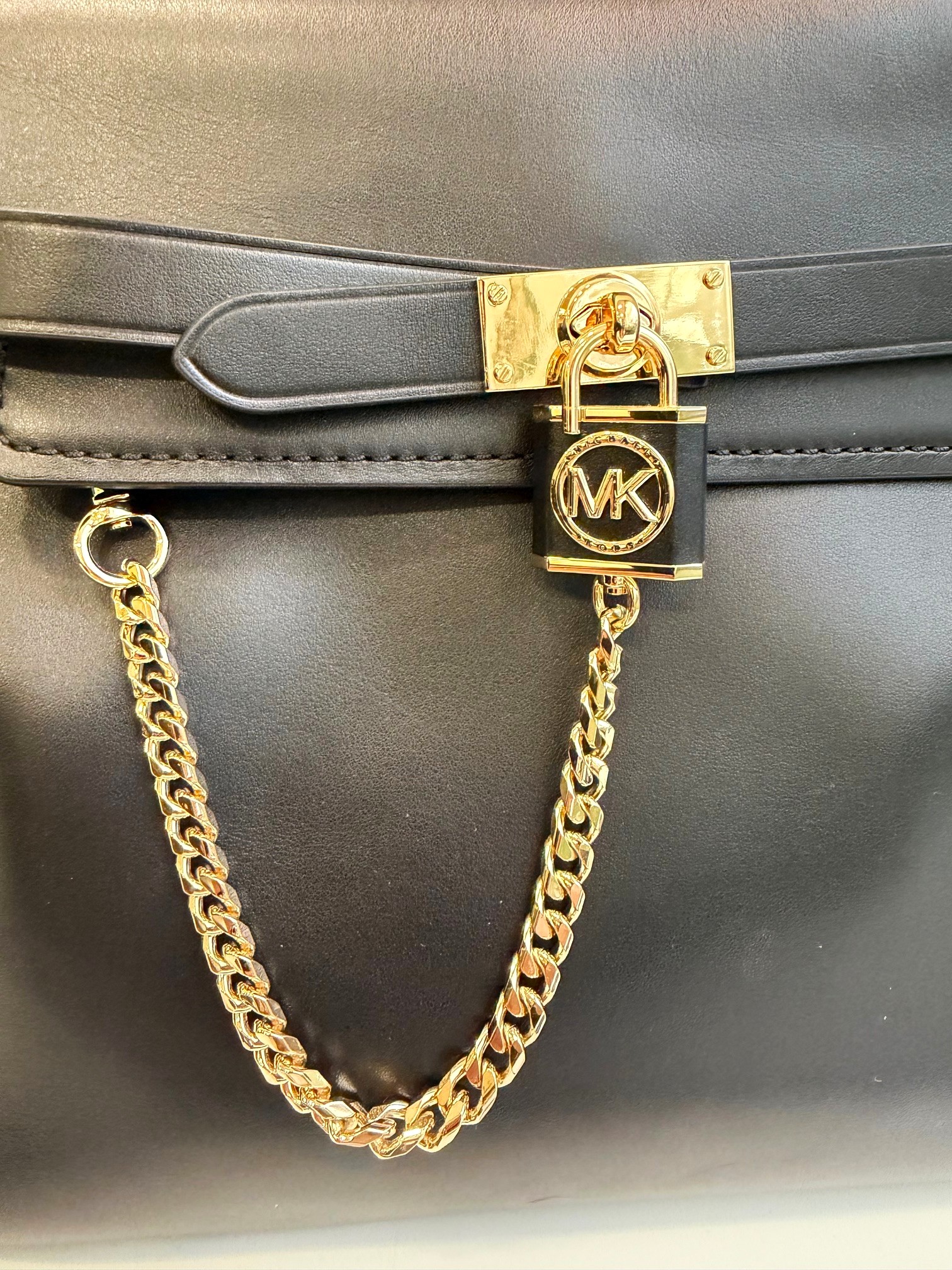 Schwarze Michael Kors Handtasche aus Leder mit goldfarbenen Details, MK-Schloss und Kette, Schnappverschluss, abnehmbarem Schultergurt, Maße 34x23x17cm, elegantes Design, leichte Gebrauchsspuren sichtbar.