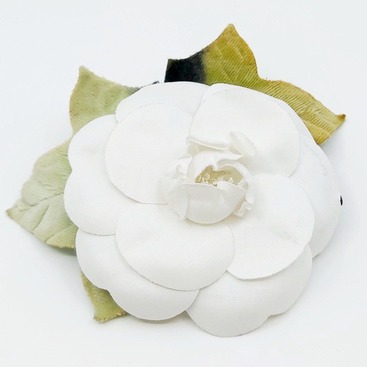 Chanel Camelia Brosche von 1995, gefertigt aus weißem Nylon und Feincord, ca. 9 cm Durchmesser, detailreiche Blüte mit grünen Blättern, elegante Vintage-Accessoire für Damen, auf weißem Hintergrund.